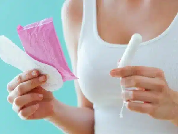 mulher segurando tampão vaginal e absorventes intimos, simbolizando as oscilações hormonais que causam a coceira genital
