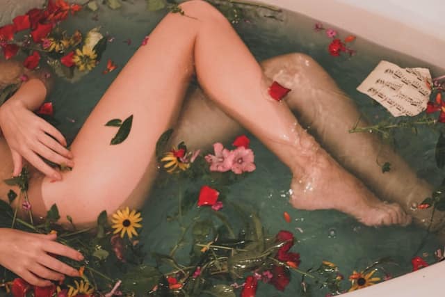 Mulher na banheira fazendo banho de beleza com flores e folhas