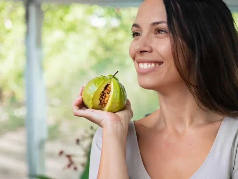 mulher sorridente segurando a fruta da goiabeira