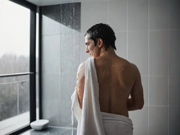 fotod e um homem com candidíase cutânea saindo do banho enrolado na toalha e observando pela janela